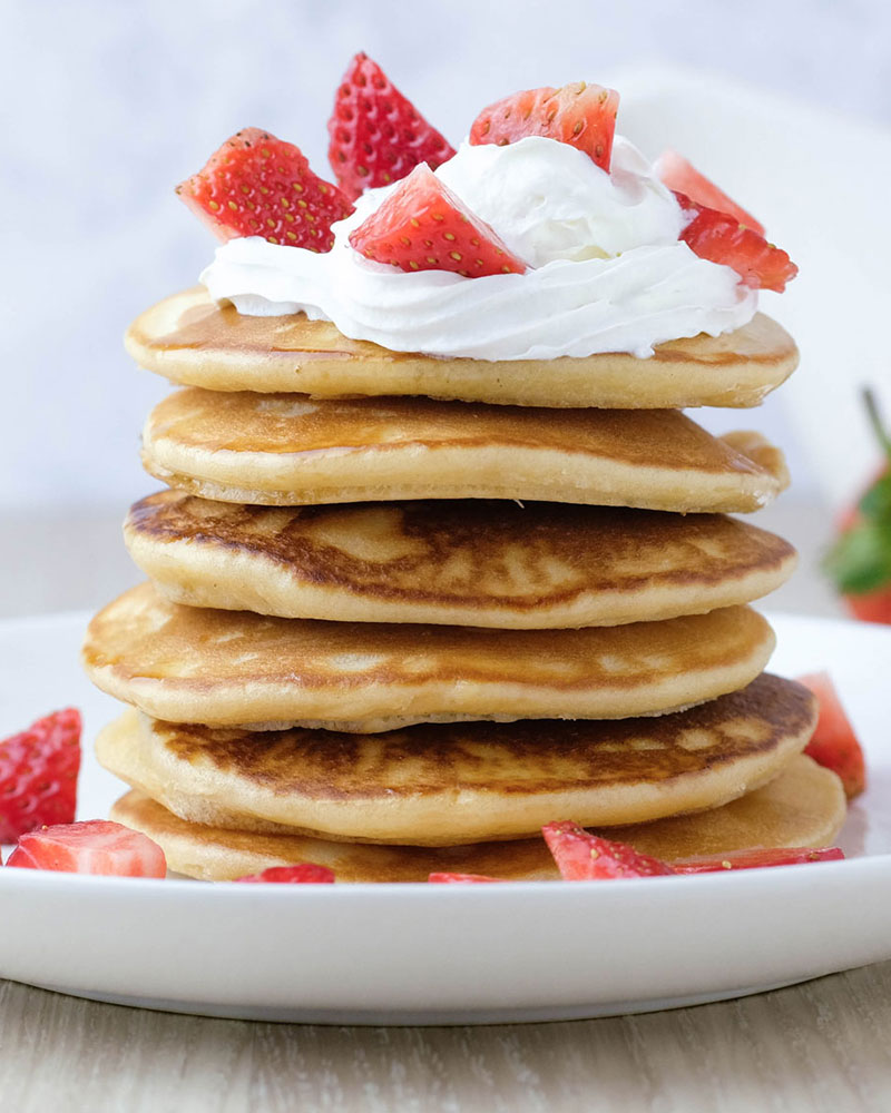 A stack of small kosher pancakes topped with whipped cream and strawberries.
