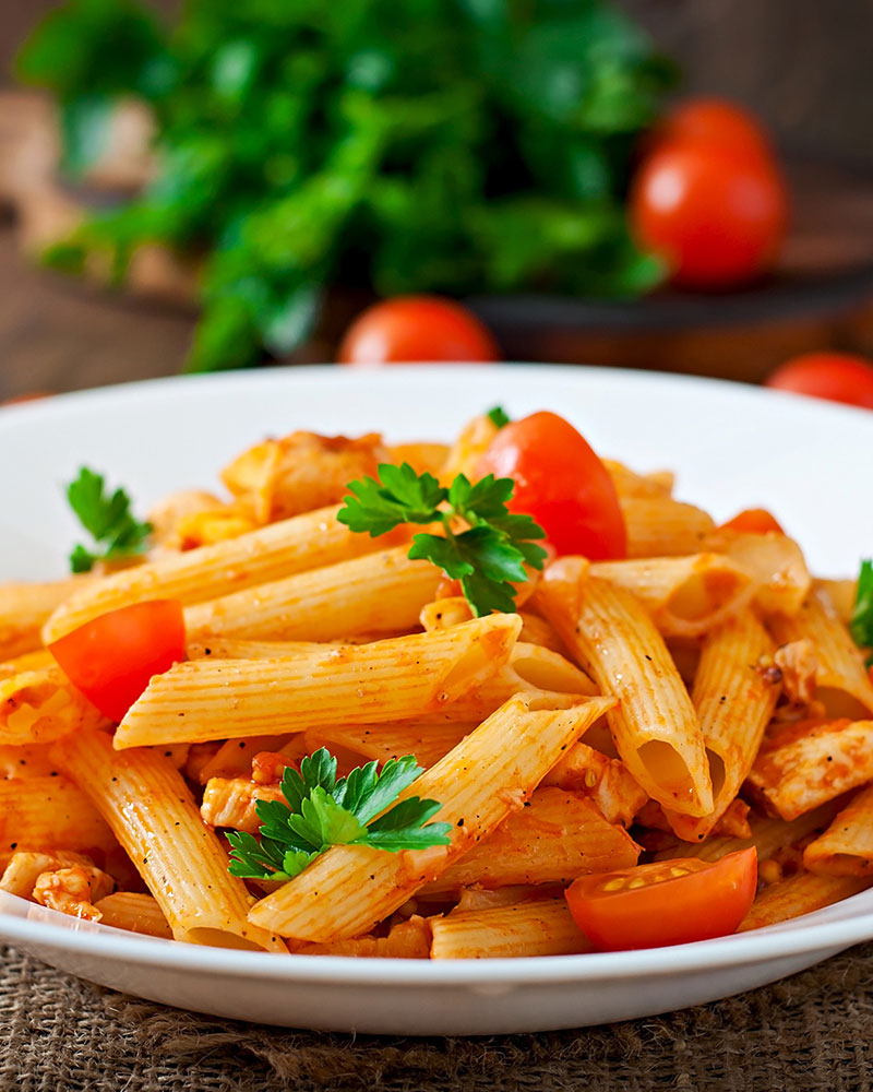 A bowl of penne pasta in vodka sauce with tomatoes and fresh parsley.